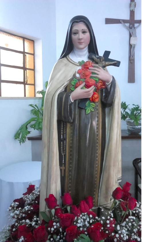 Imagem de Santa Teresinha em gesso, com crucifixo e rosas.